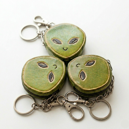 Three green alien-shaped keychains on a white background